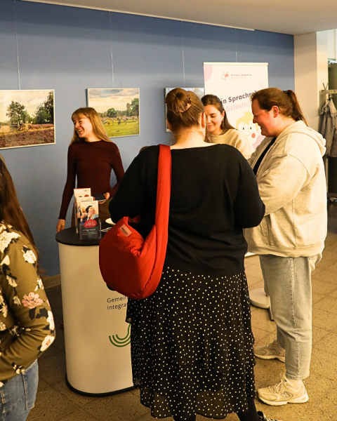Einige Menschen stehen in einem Foyer vor einem GiB-Infostand. Sie unterhalten sich angeregt.