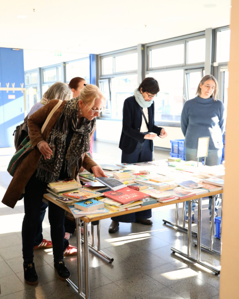 Mehrere Personen sind im Foyer vor einem Büchertisch. Eine Person greift gerade nach einem Buch.