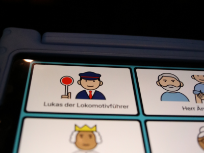 Das Bild zeigt ein Tablet, auf dem Motive von dem Schauspielstück sind. Links oben ist Lukas, der Lokomotivführer, als Piktogramm und mit Text.
